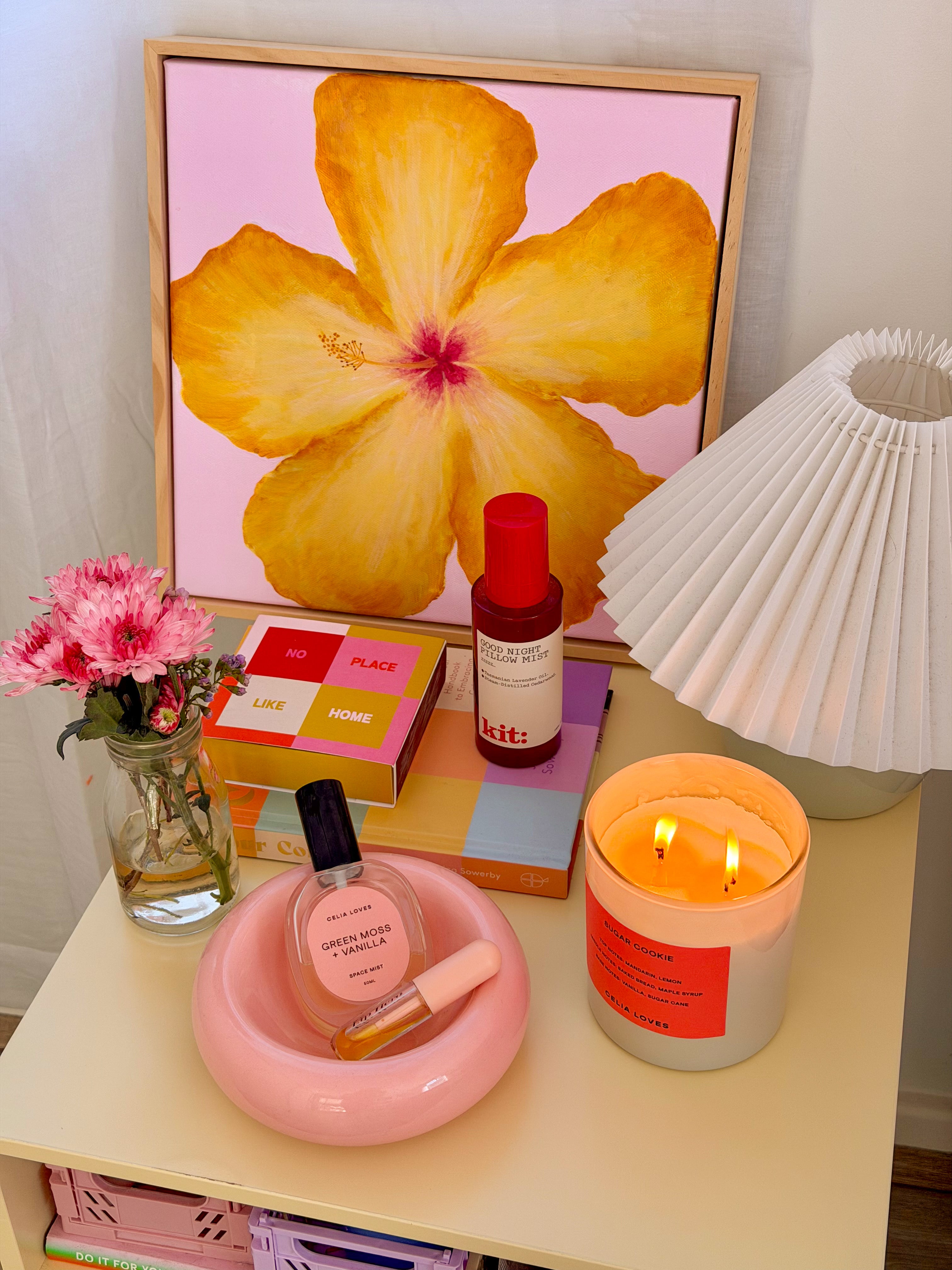 Decorative table with a candle, flowers, and a painting of a yellow hibiscus flower.